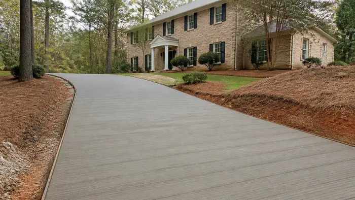 A broom drags across a driveway creating a slip-resistant texture. at a tan-brick colonial in Lawrenceville, GA, under bright midday cloud.