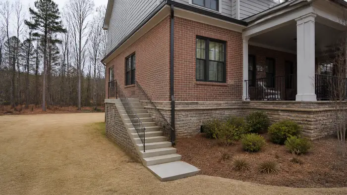 Concrete exterior stairs with a pipe handrail leading to a side entry at a brick-and-siding two-story home in Lawrenceville, GA, under an overcast sky.
