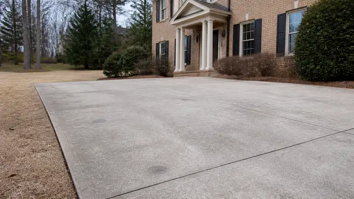 Concrete slab leveled with small patched holes from mudjacking at a tan-brick colonial in Lawrenceville, GA, under bright midday cloud.