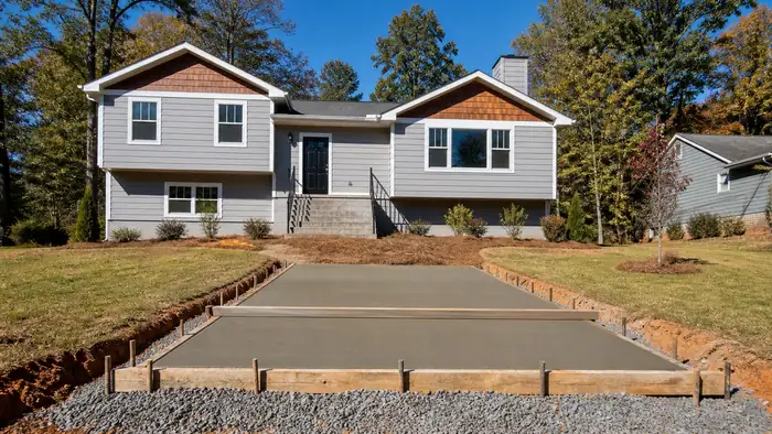 A screed board levels fresh concrete on a small patio. at a grey split-level home in Lawrenceville, GA, in clear late-morning sun.