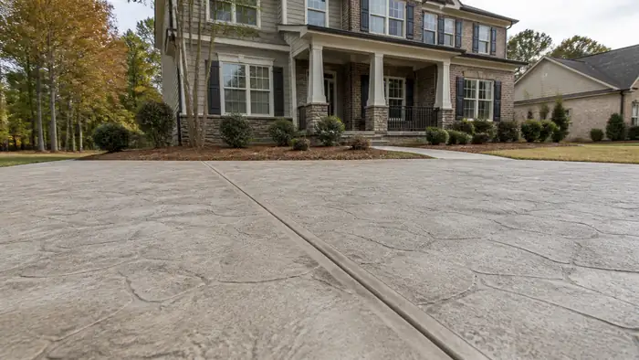 Close-up of stamped concrete texture and hand-tooled joint lines at a brick-and-siding two-story home in Lawrenceville, GA, under bright midday cloud.